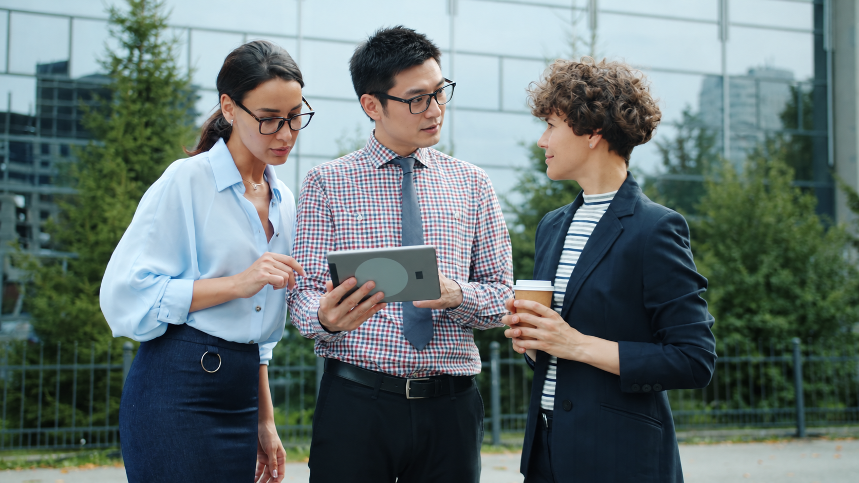 Three professionals discussing information on a tablet outside a business building
